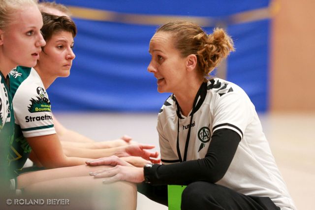 Eine Handballtrainerin spricht mit zwei Spielerinnen auf der Auswechselbank